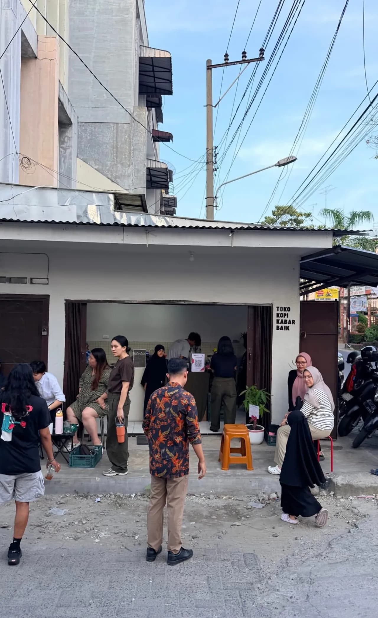 Sore hari di Toko Kopi Kabar Baik — tamu berbincang santai di depan toko